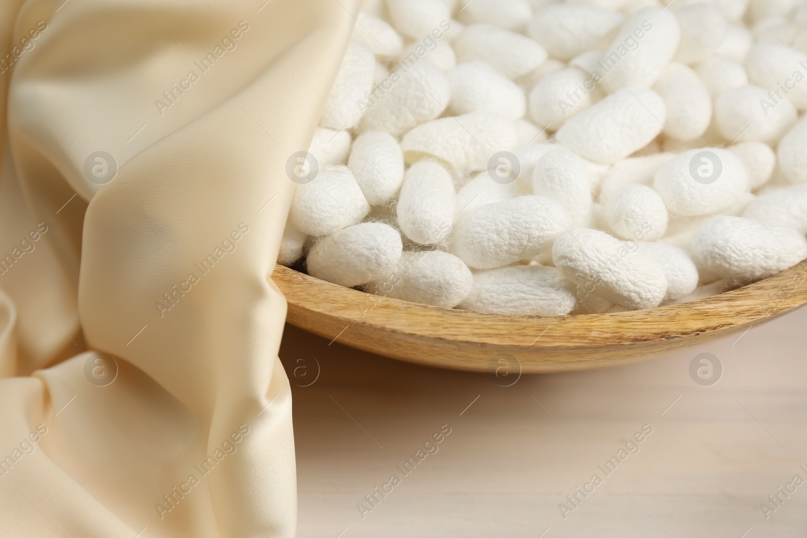 Photo of Cocoons with bowl and silk fabric on white wooden table, closeup