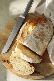 Freshly baked sourdough bread and knife on light table, top view