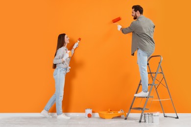 Photo of Designers painting orange wall with brush and roller indoors
