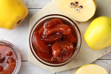 Photo of Tasty homemade quince jam in bowls and fruits on tiled table, flat lay