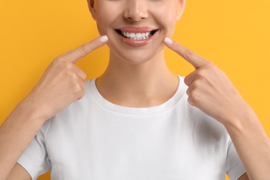 Woman showing her clean teeth and smiling on yellow background, closeup