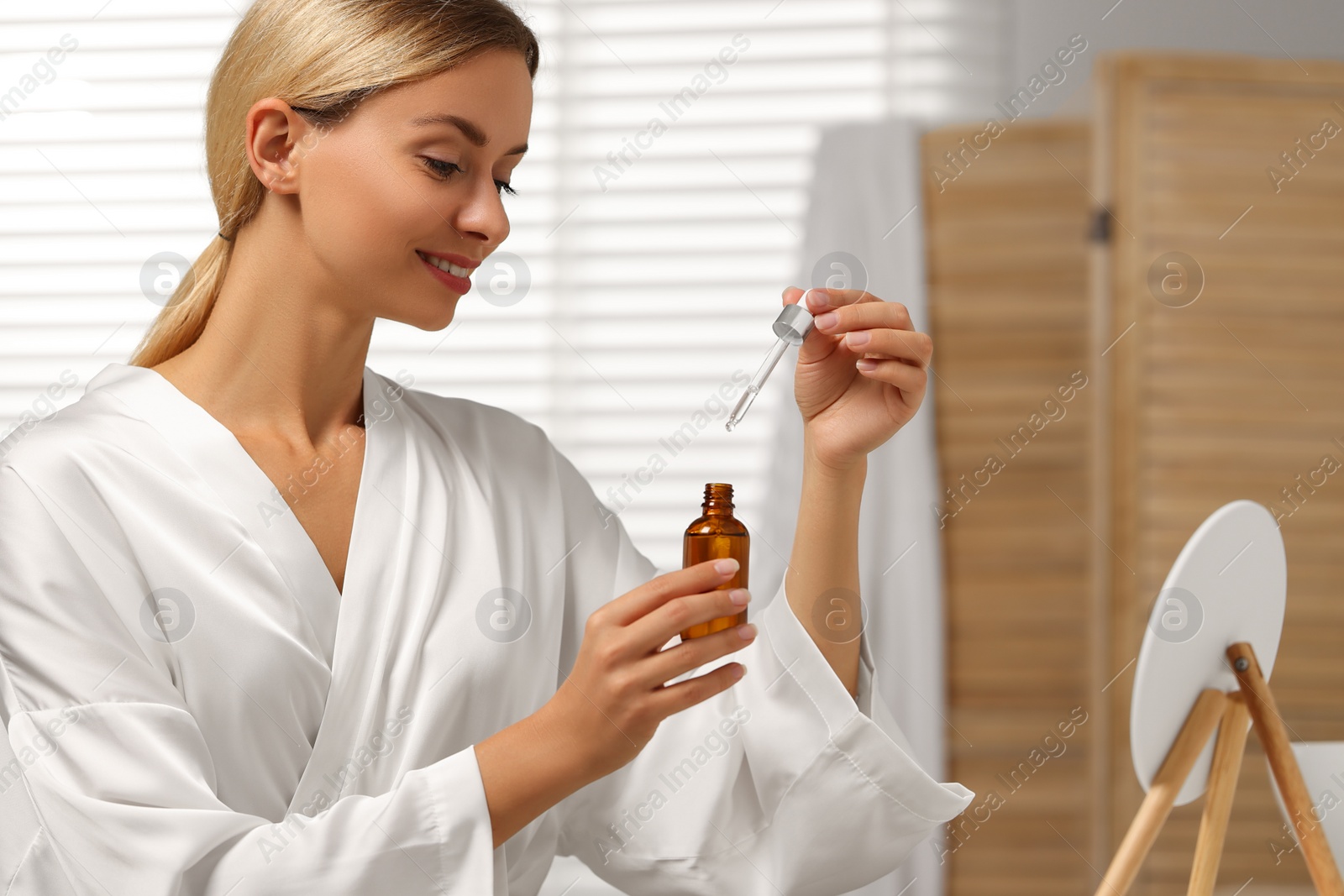 Photo of Beautiful woman with cosmetic serum in her hands in bathroom