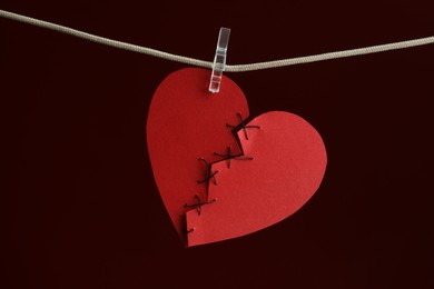Broken heart. Torn red paper heart sewed with thread on rope against burgundy background