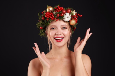 Beautiful young woman wearing Christmas wreath on black background