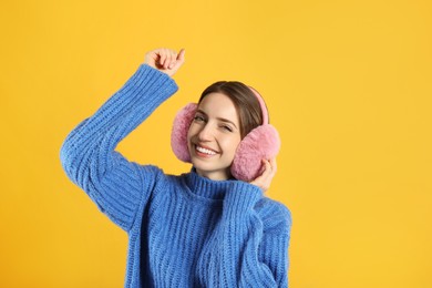 Photo of Happy woman wearing warm earmuffs on yellow background