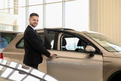 Young salesman near new car in dealership