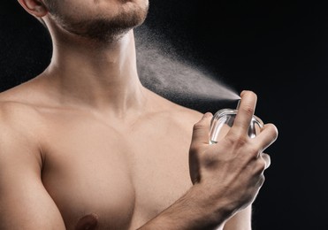Image of Handsome man applying perfume on black background, closeup