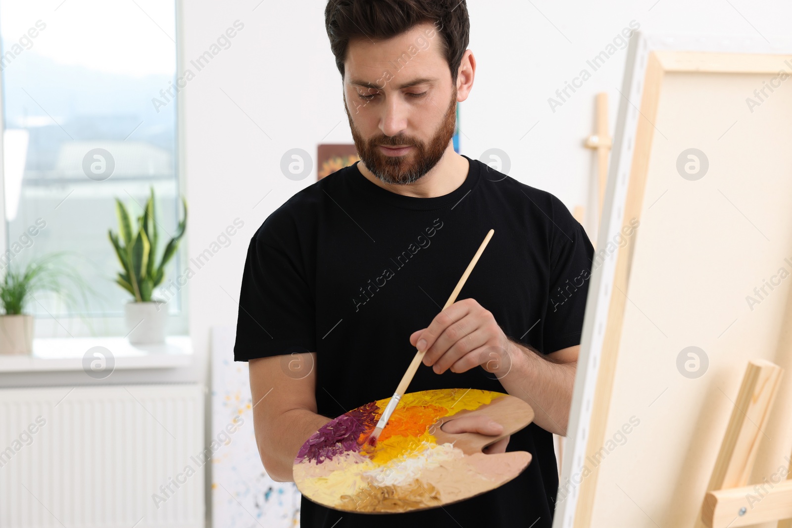 Photo of Man painting in studio. Using easel to hold canvas