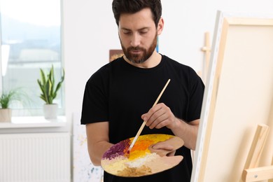 Man painting in studio. Using easel to hold canvas