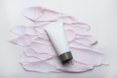 Photo of Tube and smear of pink body cream on white background, top view