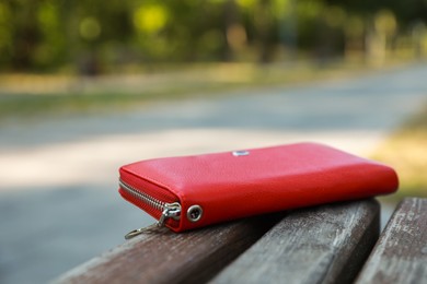 Red purse on wooden bench outdoors, space for text. Lost and found