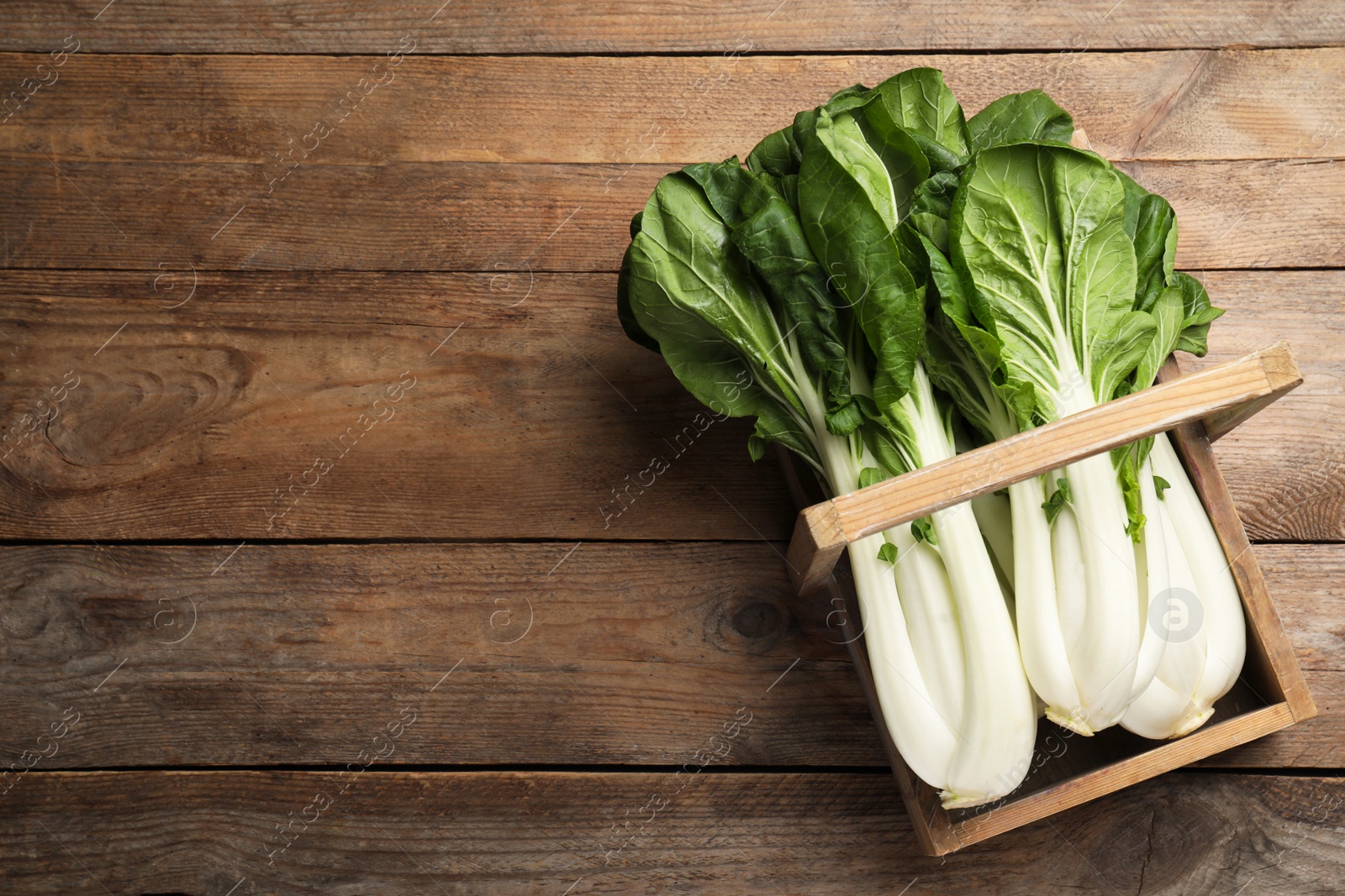 Photo of Fresh green pak choy cabbages in crate on wooden table, top view. Space for text