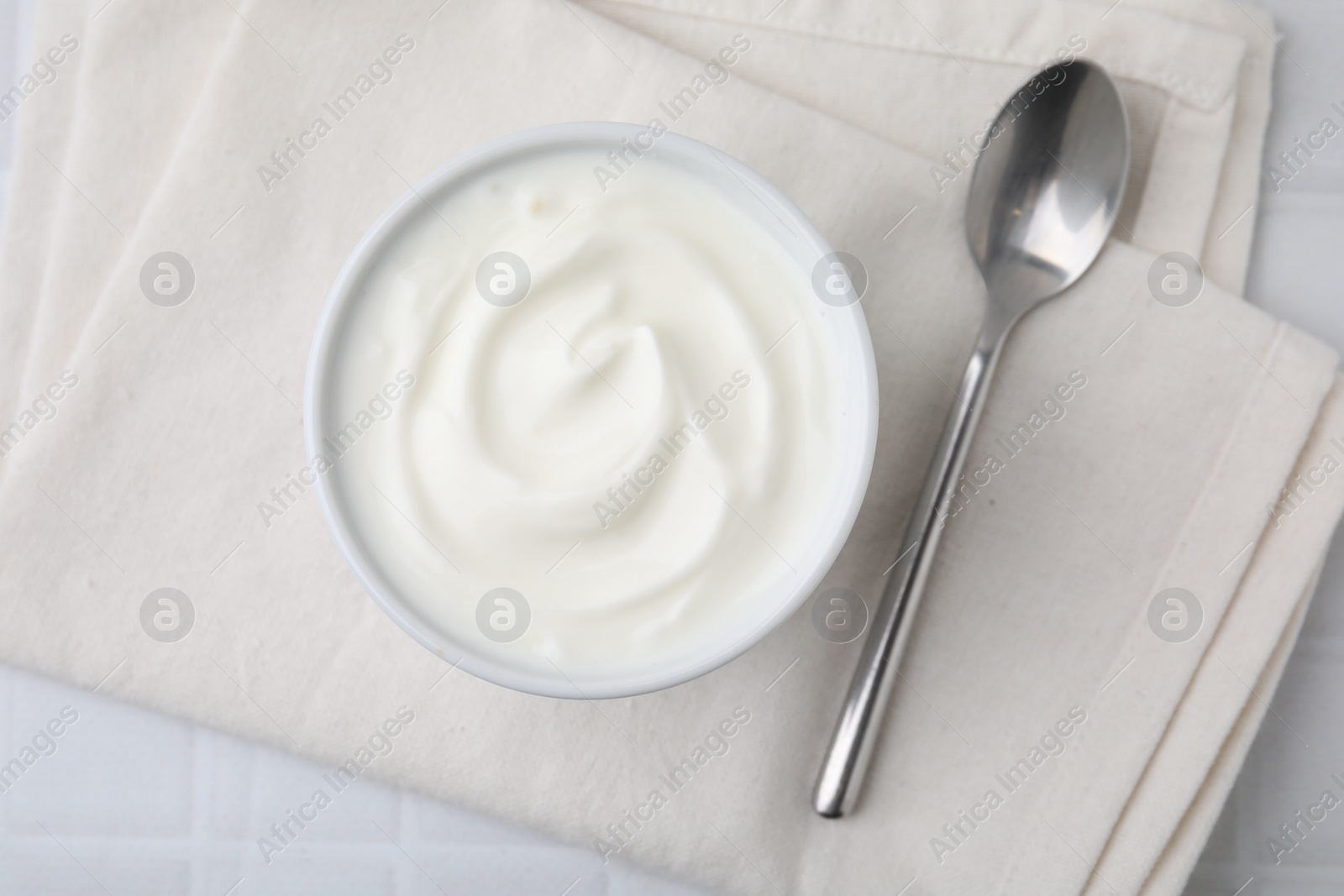 Photo of Delicious natural yogurt in bowl and spoon on white table, top view