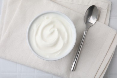 Delicious natural yogurt in bowl and spoon on white table, top view