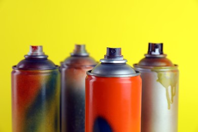 Photo of Used cans of spray paints on yellow background, closeup