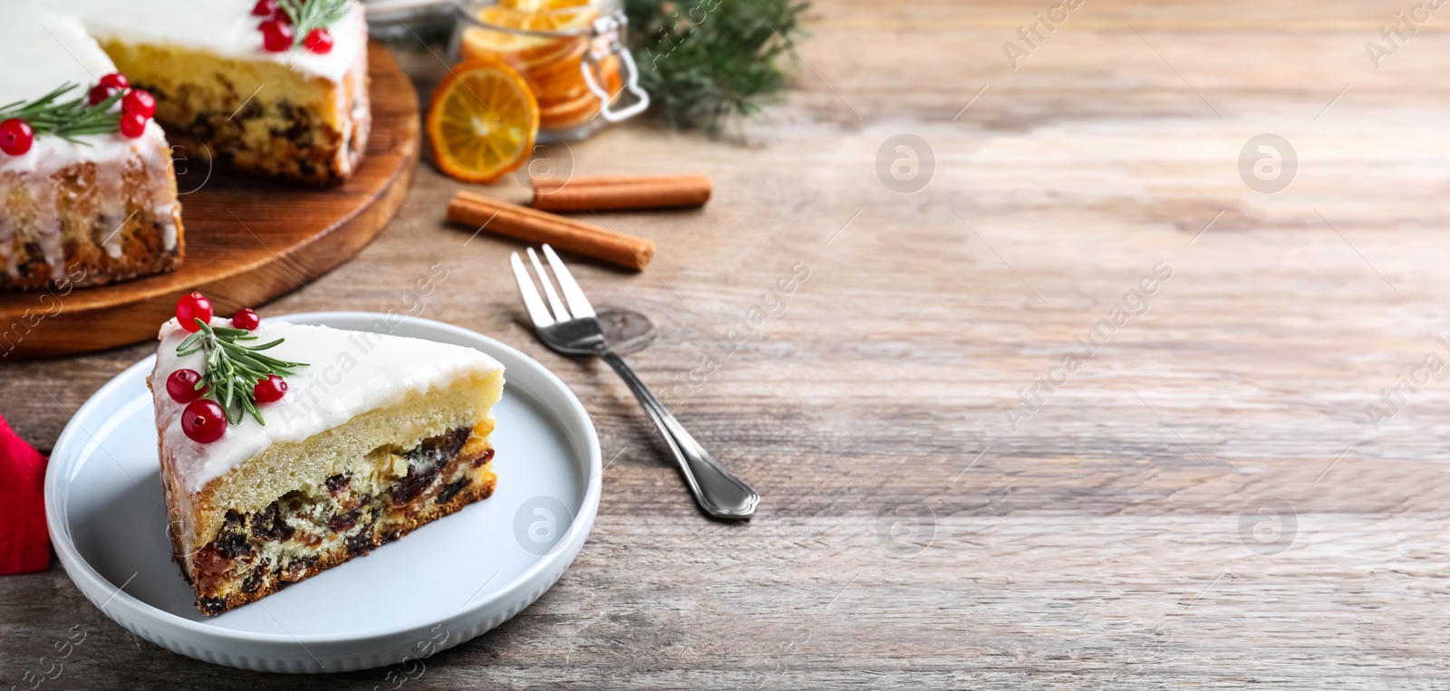 Image of Slice of traditional Christmas cake decorated with rosemary and cranberries on wooden table, space for text. Banner design