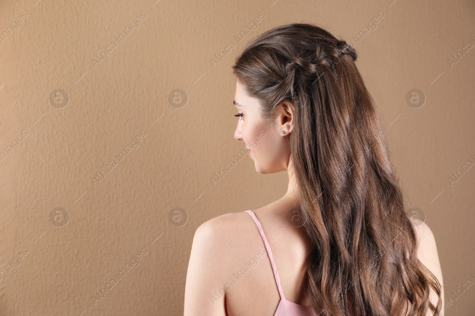 Photo of Woman with braided hair on light brown background, back view. Space for text