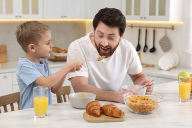 Photo of Father and his cute little son having breakfast at table in kitchen