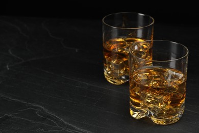 Photo of Whiskey and ice cubes in glasses on black table, closeup. Space for text