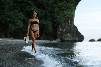 Photo of Beautiful young woman in stylish bikini on seashore, space for text