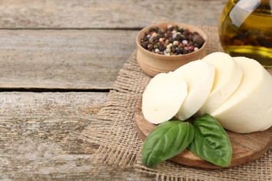 Board with tasty mozzarella slices and basil leaves on wooden table. Space for text