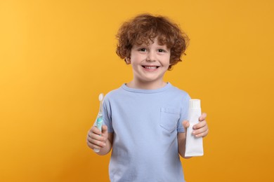 Photo of Cute little boy holding electric toothbrush and tube of toothpaste on yellow background