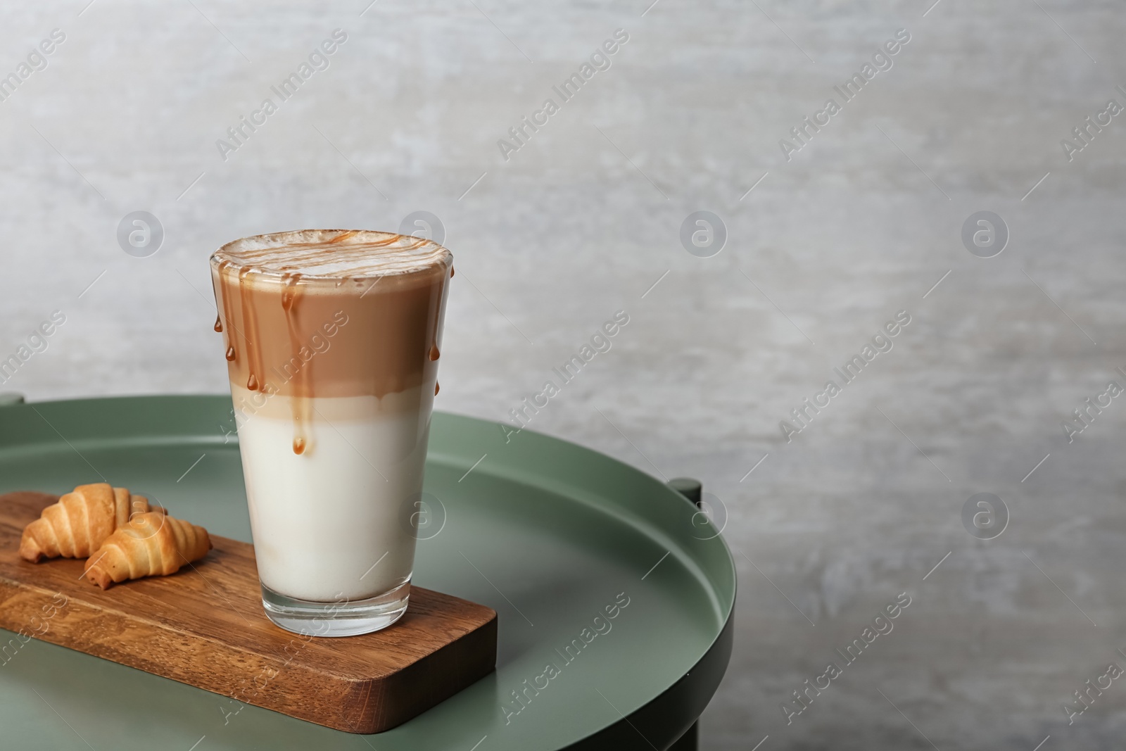 Photo of Tray with glass of caramel macchiato and tasty pastry on table, space for text