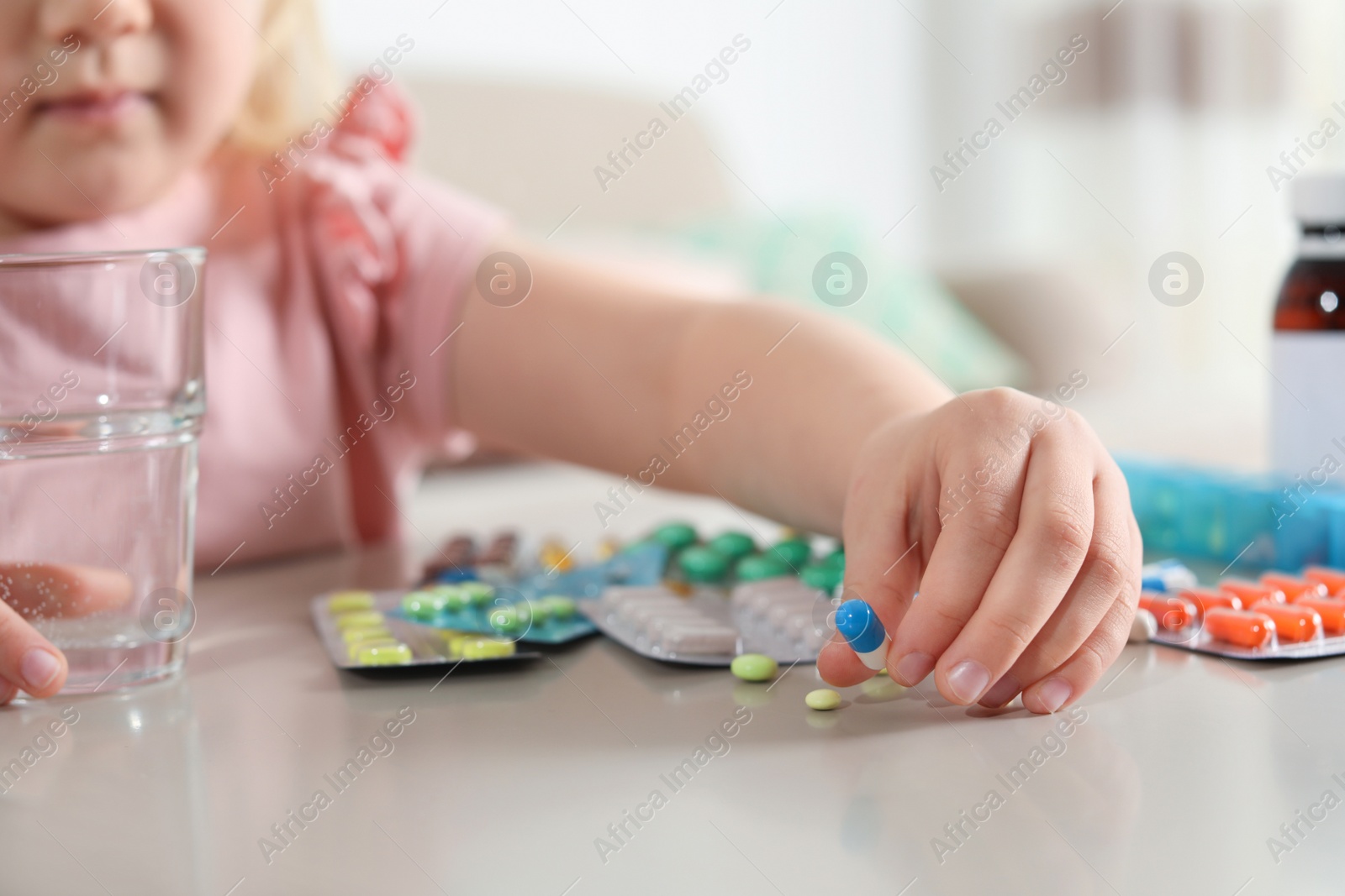 Photo of Little child with many different pills and water at table indoors, closeup. Danger of medicament intoxication