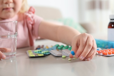 Photo of Little child with many different pills and water at table indoors, closeup. Danger of medicament intoxication