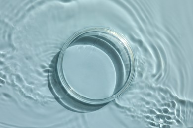 Photo of Stylish presentation for product. Glass podium in water on light blue background, top view