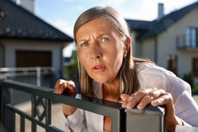 Concept of private life. Curious senior woman spying on neighbours over fence outdoors