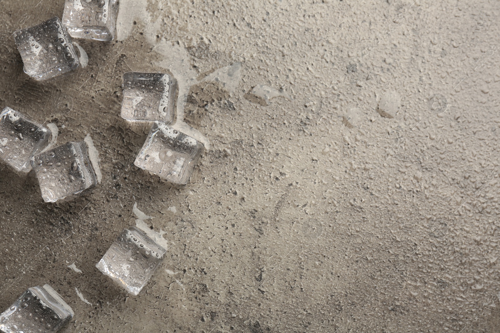 Photo of Melting ice cubes and water drops on grey textured table, flat lay. Space for text