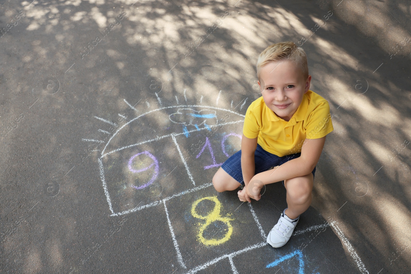 Photo of Little boy drawing hopscotch with chalk on asphalt outdoors. Happy childhood