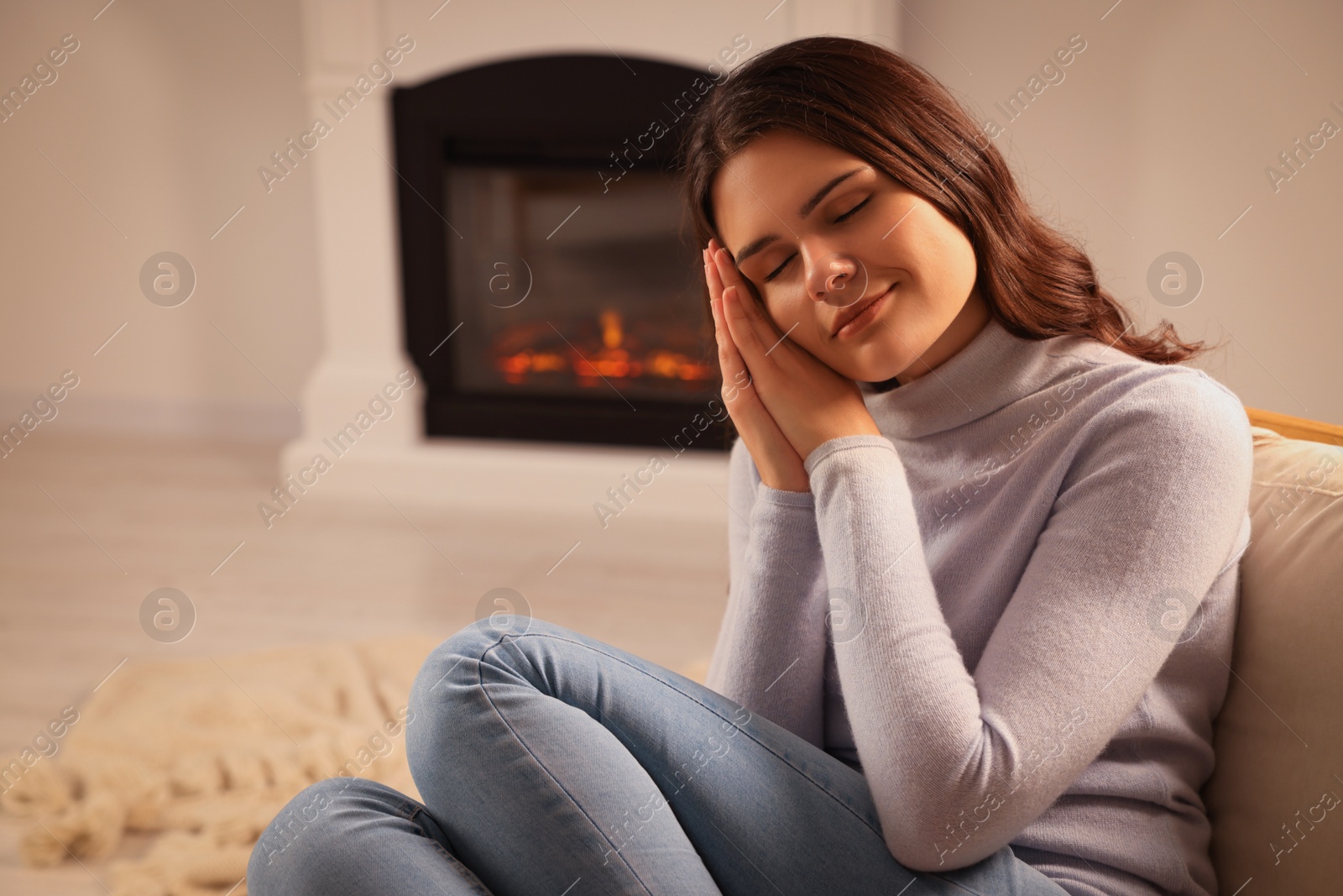 Photo of Young woman resting near fireplace at home, space for text