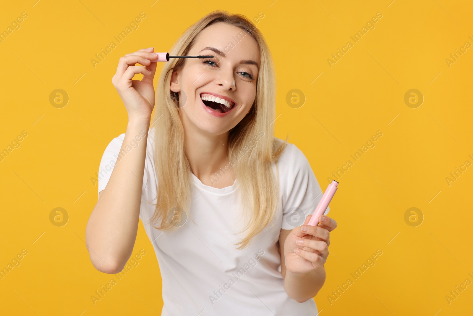 Photo of Beautiful woman applying mascara on orange background