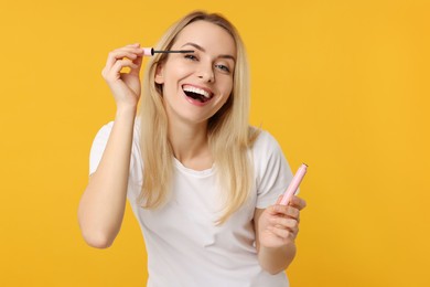 Photo of Beautiful woman applying mascara on orange background