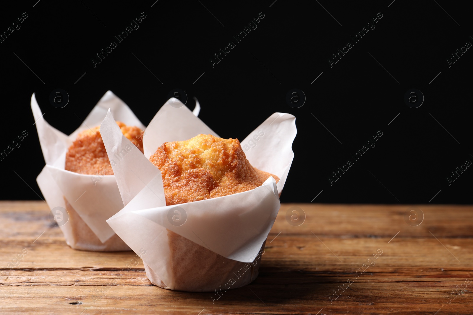 Photo of Delicious sweet muffins on wooden table against dark background, closeup. Space for text