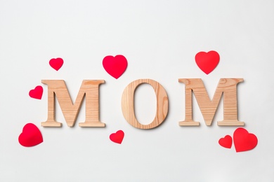 Word "MOM" made of wooden letters and paper hearts on white background. Happy Mother's Day