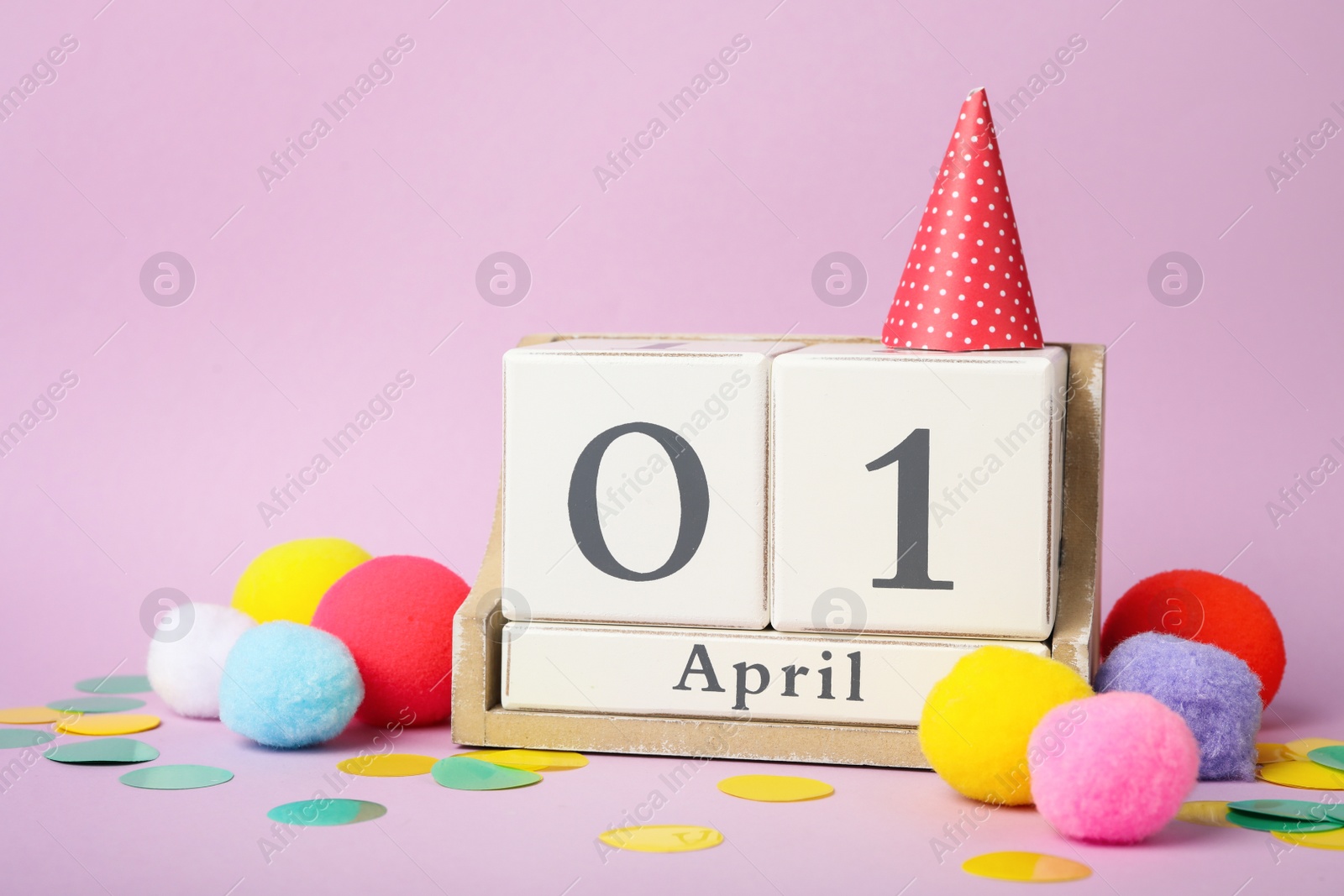 Photo of Wooden block calendar and party decor on violet background. April fool's day