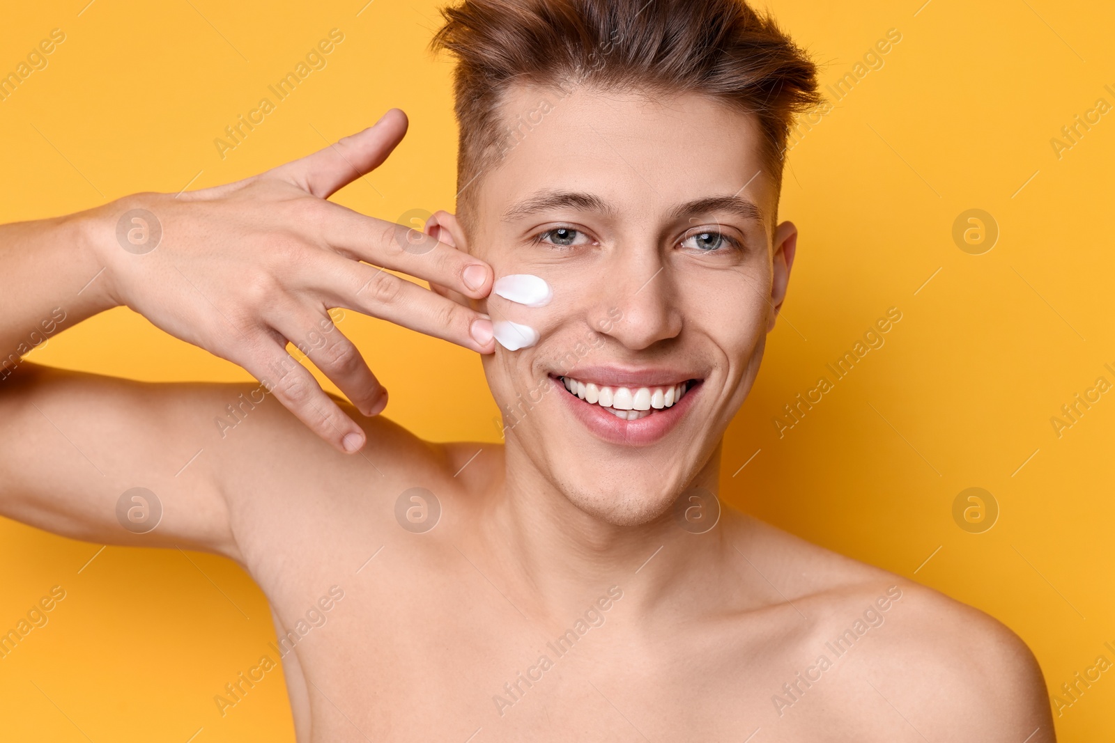 Photo of Handsome man applying moisturizing cream onto his face on orange background