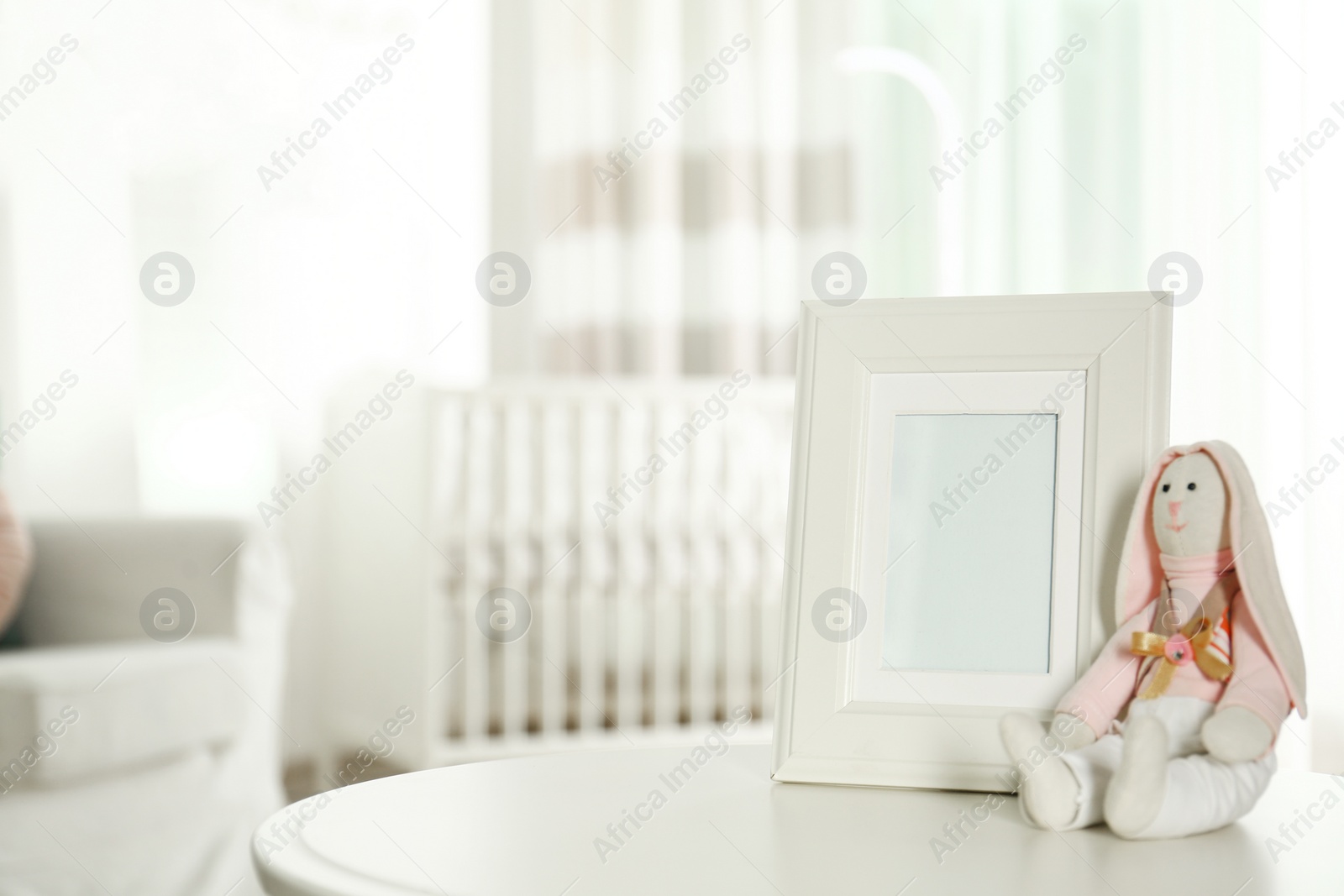 Photo of Photo frame and stuffed toy bunny on table in baby room interior. Space for text