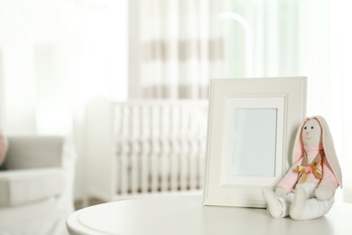 Photo of Photo frame and stuffed toy bunny on table in baby room interior. Space for text