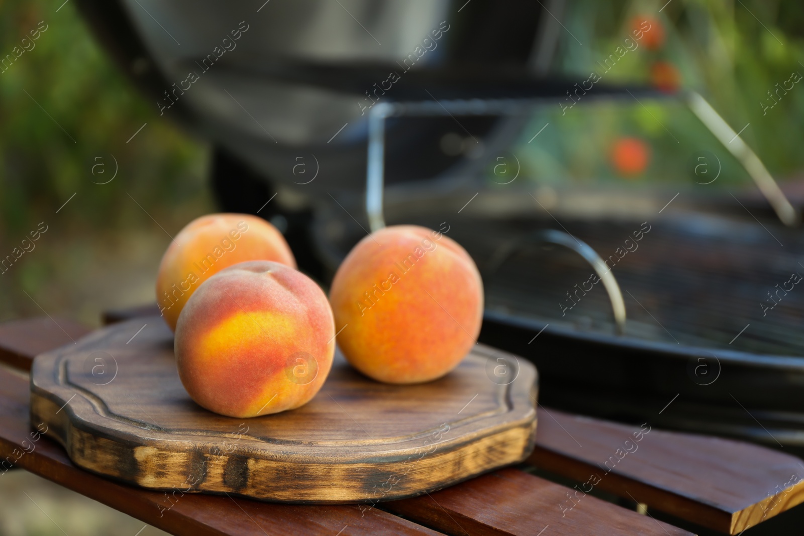 Photo of Fresh peaches on wooden table near modern grill outdoors, closeup