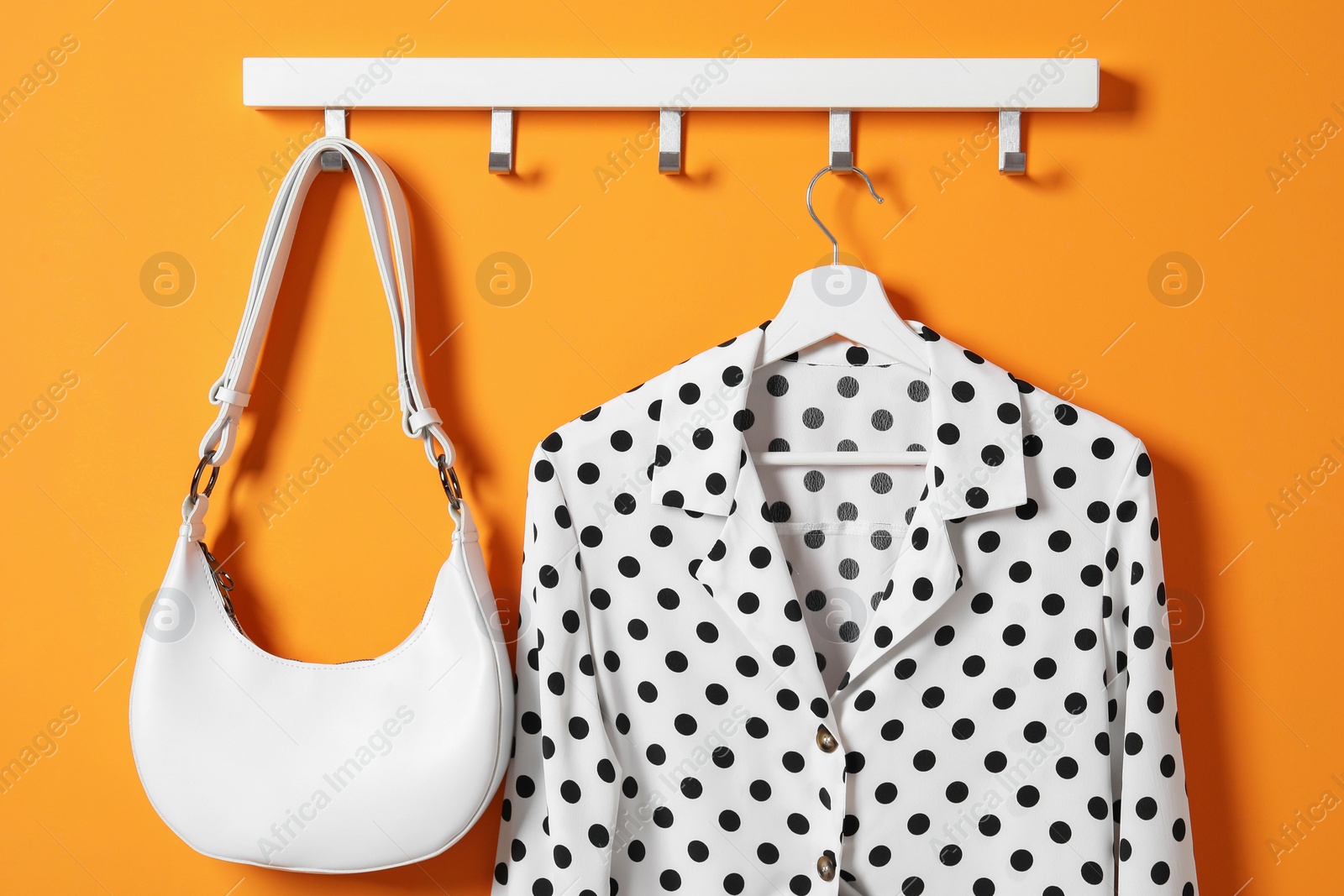 Photo of Hanger with polka dot shirt and bag on orange wall