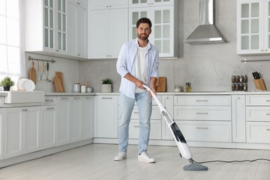 Happy man cleaning floor with steam mop in kitchen at home