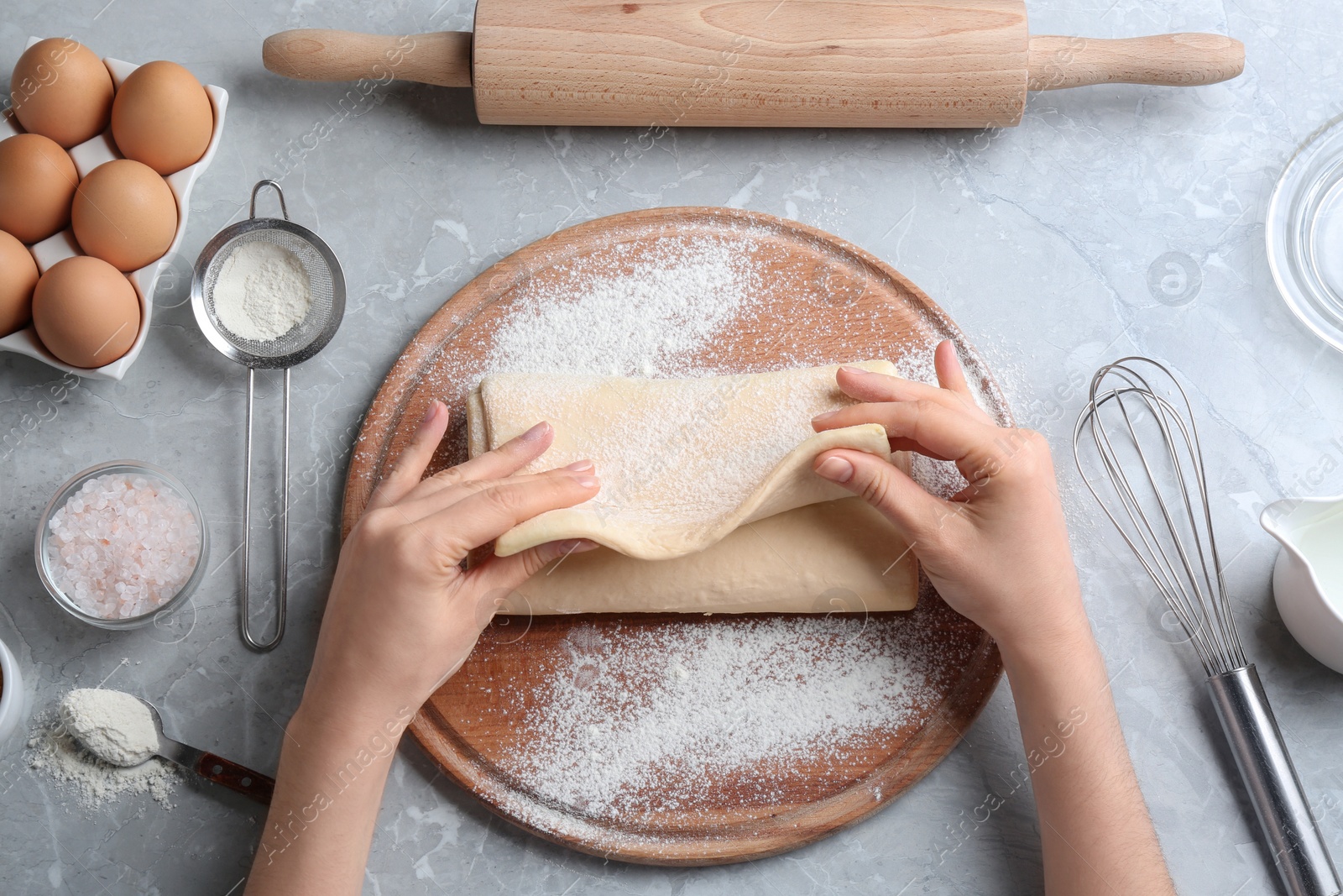 Photo of Young woman with puff pastry dough and ingredients on grey table, top view