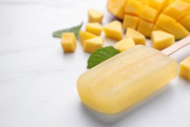 Photo of Tasty mango ice pop on white table, space for text. Fruit popsicle
