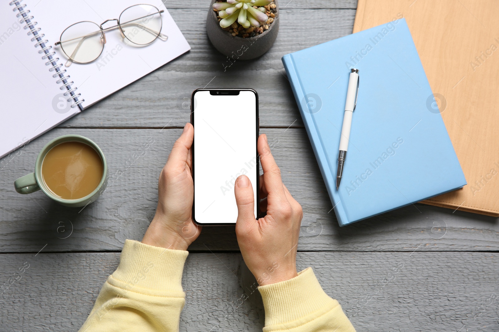 Photo of Woman with smartphone at grey wooden table, top view