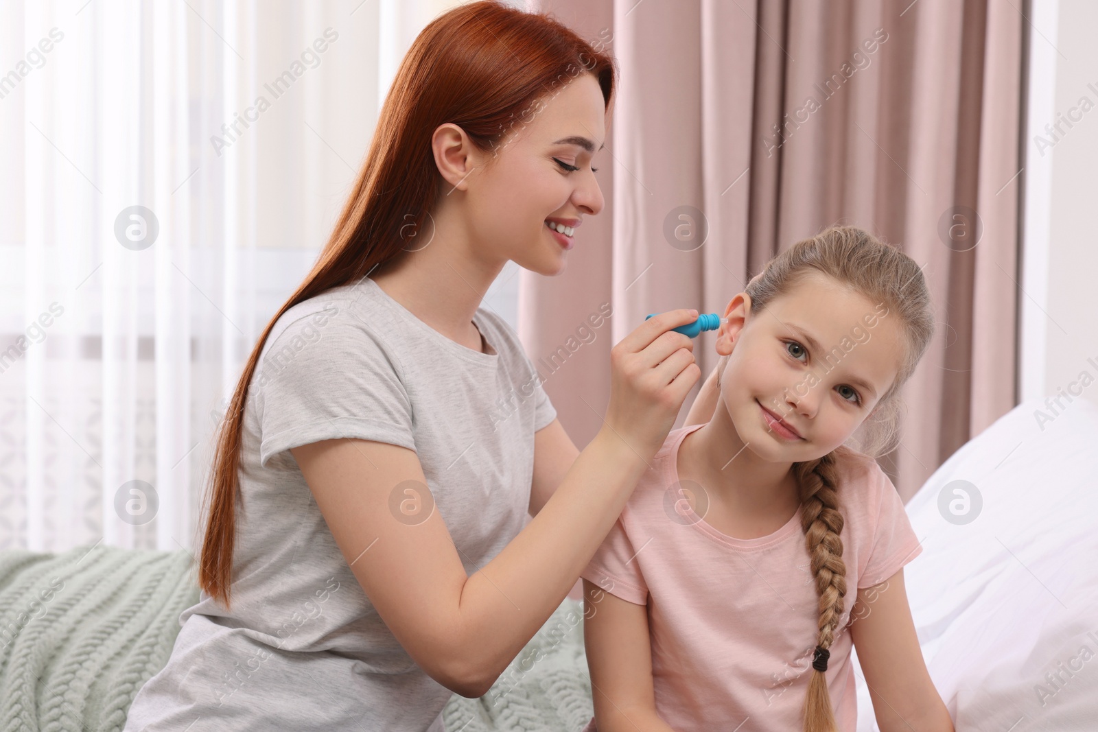 Photo of Mother dripping medication into daughter's ear in bedroom