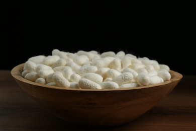 Photo of White silk cocoons in bowl on wooden table, closeup